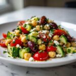 Close-up of a fresh mediterranean chickpea salad featuring chickpeas, cucumbers, tomatoes, olives, and feta.