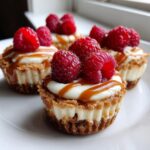 Four decadent mini cheesecake bites topped with cream, caramel drizzle, and fresh raspberries.