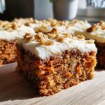 Close-up of a moist carrot cake bars slice topped with thick cream cheese frosting and walnuts.