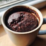 Close-up of a rich, dark chocolate mug cake topped with chocolate chips, ready to eat.