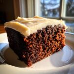 Close-up of a moist slice of dark gingerbread cake topped with thick, light-colored frosting.