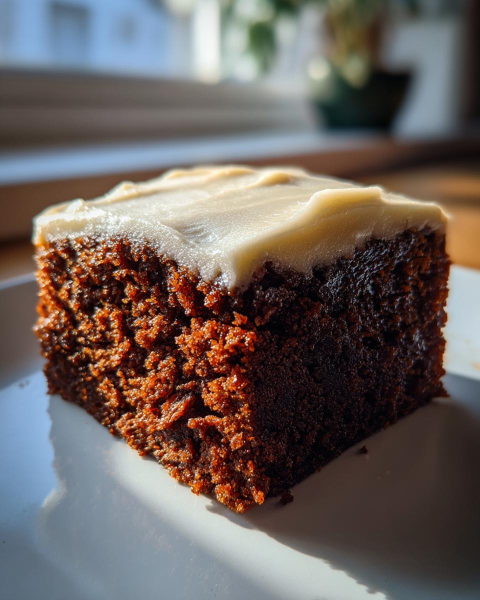 Close-up of a moist, dark slice of gingerbread cake topped with thick, creamy white frosting.
