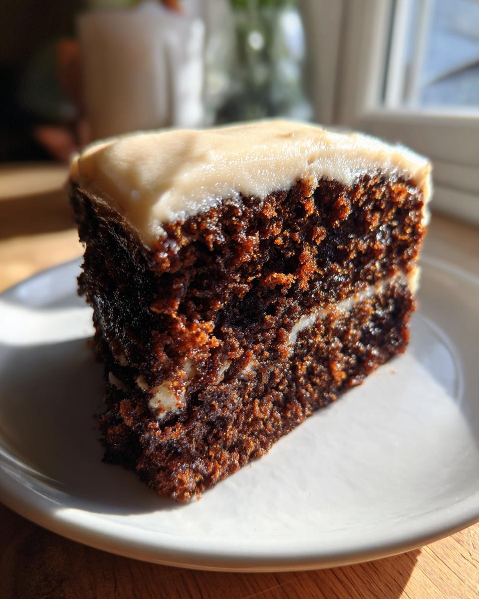 Close-up of a moist slice of dark gingerbread cake with a layer of light frosting in the middle and on top.