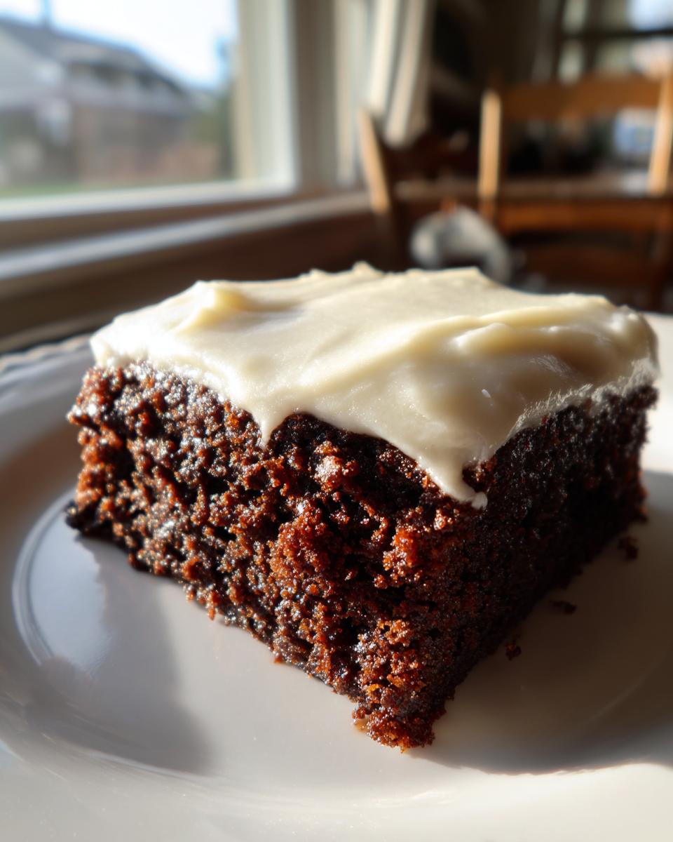 A close-up of a moist slice of dark gingerbread cake topped with thick white frosting.