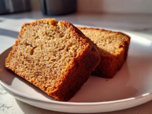 Two moist slices of golden brown greek yogurt banana bread resting on a white plate.