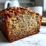 Close-up of a moist slice of sugar free banana bread showing the dark flecks of banana and topped with walnuts.