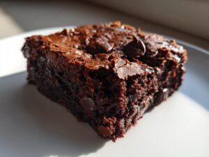 A close-up, richly textured slice of moist sweet potato brownies topped with melted chocolate chips on a white plate.
