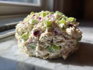 A perfectly molded scoop of creamy cottage cheese chicken salad mixed with visible chunks of celery and red onion.