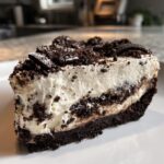 Close-up of a thick slice of no-bake Oreo pie showing dark crust, creamy white filling, and crushed cookie topping.