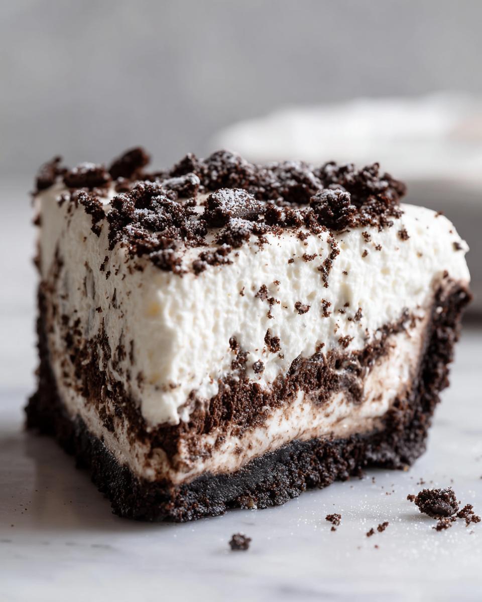 Close-up of a thick slice of no-bake Oreo pie showing a dark crust, white creamy filling, and crushed cookie topping.