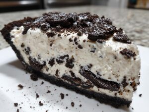 A close-up of a thick slice of no-bake Oreo pie with creamy filling and chocolate cookie crust.