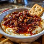 Close-up of a creamy pepper jelly cheese dip topped with candied pecans, served with a cracker.
