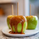 Close-up of a bright green apple covered in thick, dripping caramel sauce, ready to eat as a caramel apple.