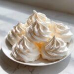 A pile of perfectly piped, crisp white meringue cookies stacked on a small white plate.