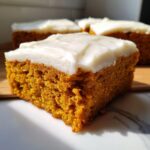 A close-up, sunlit shot of a moist square of pumpkin bars with cream cheese frosting.
