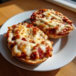 Two halves of a toasted english muffin pizza topped with melted, bubbly cheese and tomato sauce.