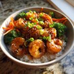 Close-up of a delicious shrimp bowl featuring glazed shrimp over white rice with broccoli and carrots, topped with green onions.