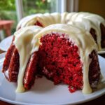 Close-up of a slice of vibrant red velvet bundt cake topped with thick, dripping cream cheese glaze.