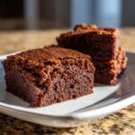 Two moist, dark chocolate squares of gingerbread brownies resting on a white plate.