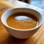 A close-up of rich, smooth turkey gravy served in a small white bowl on a wooden surface.