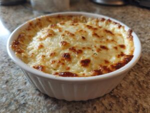 Close-up of a creamy, baked savory bread dip topped with golden-brown melted cheese in a white ramekin.