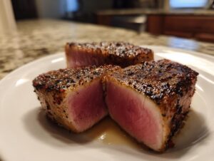Close-up of three perfectly seared tuna steak pieces, showing a rare pink center and a dark pepper crust.