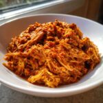 Close-up of rich, saucy shredded chicken tinga piled high in a white bowl, ready to serve.