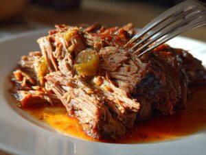 Close-up of tender, shredded Mississippi pot roast served on a white plate with savory juices and pepperoncini.