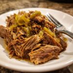 Close-up of shredded Mississippi pot roast topped with tangy pepperoncini peppers served on a white plate.