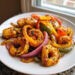Close-up of perfectly seasoned shrimp fajitas mixed with sliced red onion and bell peppers on a white plate.