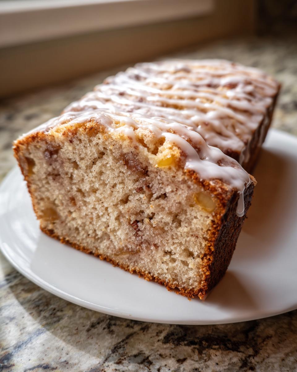 A thick slice cut from a loaf of apple fritter bread, drizzled with white icing.