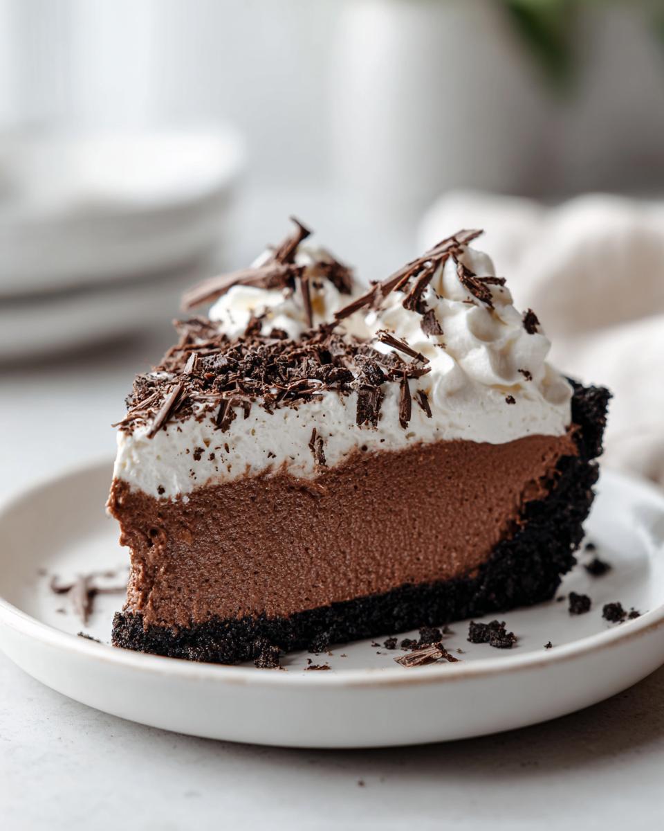A decadent slice of chocolate mousse pie featuring a dark crust, thick chocolate filling, and topped with whipped cream and chocolate shavings.
