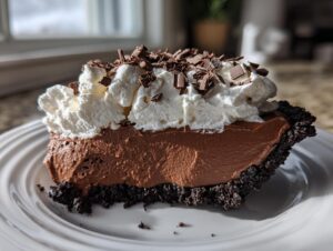 A decadent slice of chocolate mousse pie with a dark crust, topped with whipped cream and chocolate shavings.