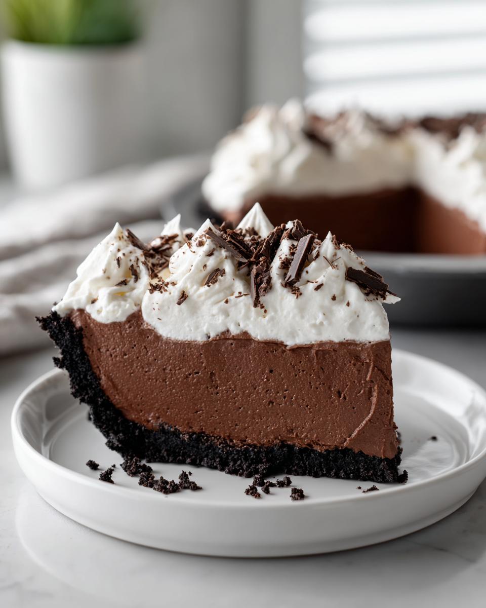 A perfect slice of decadent chocolate mousse pie with a dark crust, topped with whipped cream and chocolate shavings.