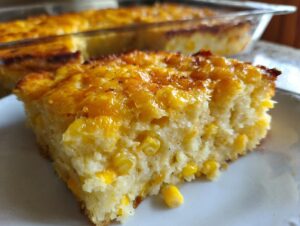 A close-up of a moist slice of cream cheese corn casserole with a golden, slightly browned top, served on a white plate.