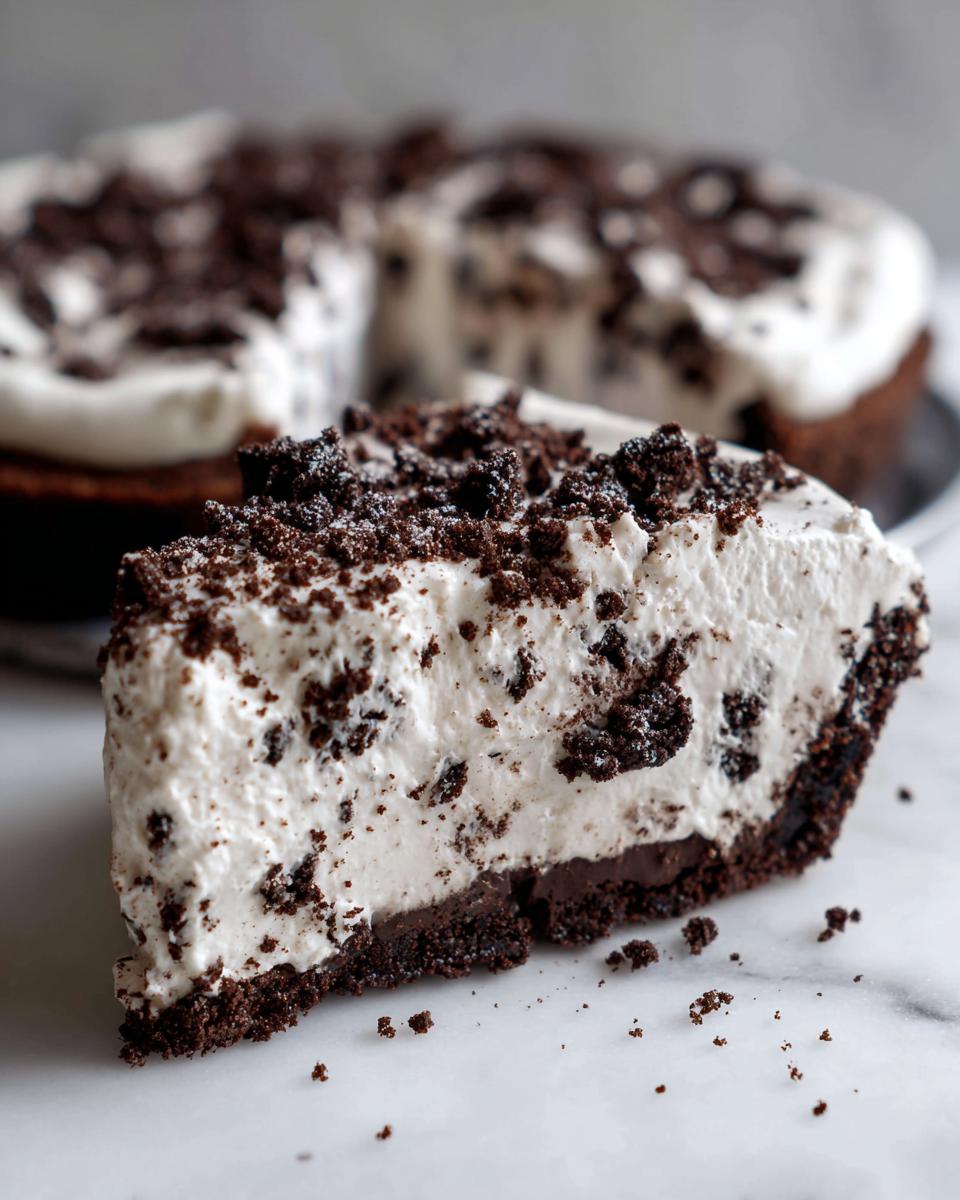 A close-up slice of no-bake Oreo pie showing the dark crust, creamy filling mixed with cookie pieces, and crumb topping.