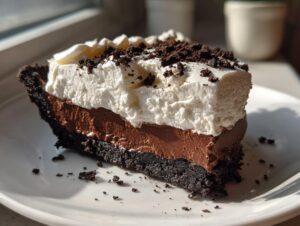 A close-up slice of rich chocolate mud pie showing a dark crust, chocolate mousse layer, and thick whipped cream topping with cookie crumbs.