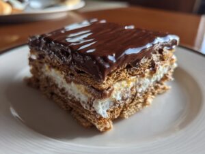 A close-up slice of layered eclair cake featuring graham crackers, cream filling, and glossy chocolate frosting.