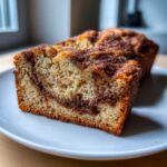 Close-up of a thick slice of snickerdoodle banana bread showing a moist crumb and dark cinnamon swirl topping.