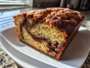 A close-up slice of moist snickerdoodle banana bread featuring a visible cinnamon swirl and sugary topping.