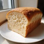 A freshly baked, golden-crusted sourdough sandwich bread loaf sliced to show its soft, airy interior crumb.