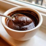 A spoonful of thick, rich homemade chocolate pudding being lifted from a white bowl.