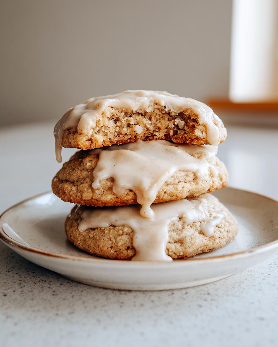 Three soft maple cookies stacked, drizzled generously with brown butter icing; the top cookie is broken open.