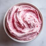 Overhead view of creamy, pink strawberry cheesecake dip swirled beautifully in a white bowl.