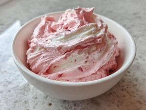 A close-up of fluffy, swirled pink and white strawberry cheesecake dip served in a small white bowl.