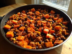 A close-up view of a savory sweet potato skillet mixture featuring ground meat, black beans, and corn.