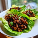 Close-up of three fresh chicken lettuce wraps filled with savory ground chicken mixture and topped with green onions.