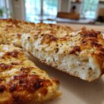 Close-up of a thick slice of white pizza showing a fluffy crust and creamy, browned cheese topping.