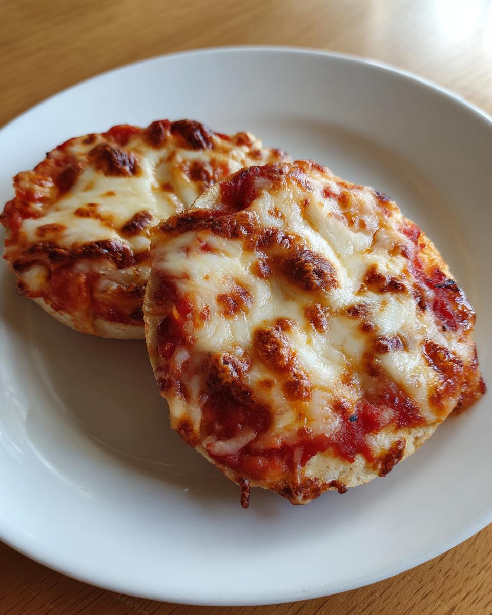 Two perfectly melted english muffin pizza halves topped with tomato sauce and browned mozzarella cheese, served on a white plate.