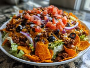A close-up of a hearty ultimate easy taco salad featuring seasoned ground beef, lettuce, cheese, tomatoes, olives, and red onion.
